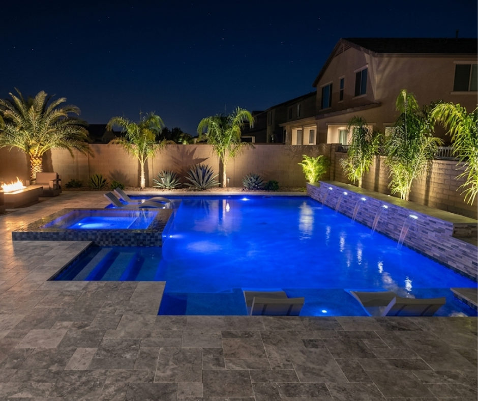 night time in the backyard with the pool all lit up with all the lights around the trees as well showing off all the best features of the backyard.